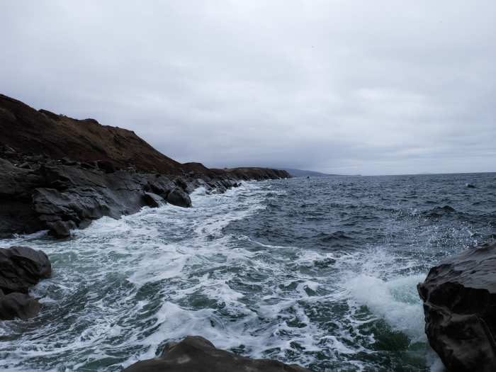 waves crash against rocks under a cloudy sky during the daytime